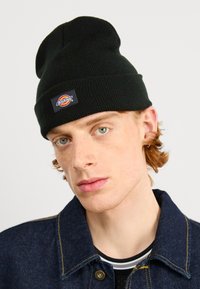 Sort strikket beanie med en foldet manchet, der har en rektangulær label med et flerfarvet logo. Blød tekstur, tætsiddende design.