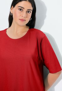 Top rosso a maniche corte in tessuto morbido. Presenta un colletto rotondo e una vestibilità comoda. Textura liscia, senza motivi visibili o decorazioni.