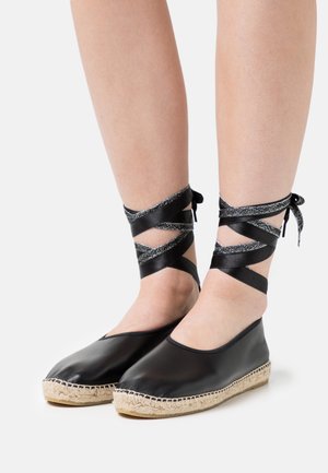 Espadrilhas em couro preto com sola de juta, apresentando fita metálica prata para atar no tornozelo, design elegante e textura suave.
