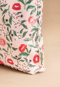 Ziedu soma ar rozā fonu, kurā attēloti sarkani lūpas un zaļas lapas. Sānu etiķete lasāma "Cath Kidston London." Taisnstūrveida forma, gluda tekstūra.