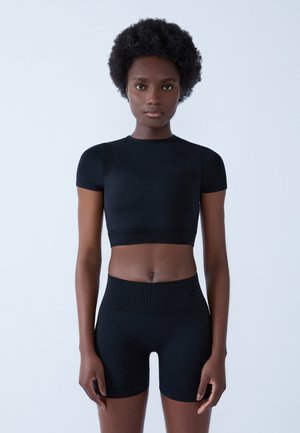 Czarny sportowy biustonosz z krótkimi rękawami, z teksturowanym wzorem. W zestawieniu z czarnymi szortami o wysokim stanie, wykonanymi z podobnego materiału.