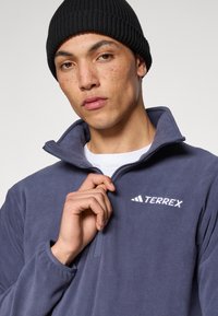 Bluza Terrex z polaru w głębokim niebieskim kolorze, z wysokim kołnierzem i suwakiem do kwadratu. Posiada białe logo na piersi oraz ściągacze na mankietach.