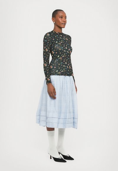 Top negru cu mânecă lungă, cu imprimeu floral multicolor; fustă midi pliată de un albastru deschis; ciorapi albi până la genunchi; tocuri negre ascuțite.