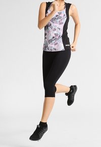 Completo sportivo nero composto da un top senza maniche con un motivo geometrico multicolore, legging neri e scarpe da ginnastica nere con accenti bianchi.