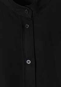 Schwarzes Button-Up-Hemd mit rundem Ausschnitt, fünf passenden Knöpfen und einer glatten Stoffoberfläche mit sichtbaren Nähten.