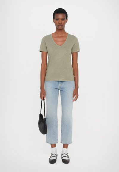 Olivgrön kortärmad t-shirt med v-ringning, kombinerad med ljusblå cropped jeans. Svart vävd handväska och grå skor med vita strumpor.