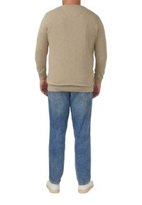 Beiger Pullover mit langen Ärmeln und Rundhalsausschnitt, kombiniert mit hellblauen Jeans und weißen Schuhen. Der Pullover hat eine strukturierte Oberfläche.