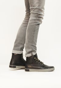 Zapatos de cuero negros de caña alta con suelas de goma gris, que cuentan con ojales metálicos y cordones en contraste, combinados con jeans ajustados gris.