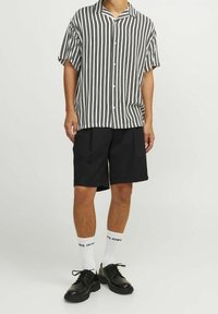 Osoba oblečená v černobílém proužkovaném krátkém rukávu s knoflíky, černých šortkách do kolen, bílých značkových ponožkách a černých kožených botách.