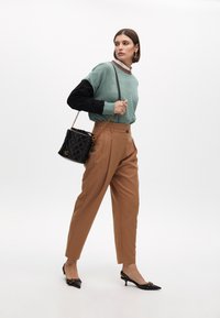 Světle zelený a černý svetr, hnědé přizpůsobené kalhoty, černá prošívaná kabelka s zlatými detaily a černé sandály na podpatku se cvočky.