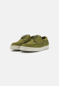 Green canvas sneakers with rounded toes, lace-up design, and light-colored soles. Features stitched accents and side grommets.