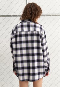 Camicia di flanella a maniche lunghe con un motivo a quadri viola, nero e bianco. Realizzata in tessuto morbido con polsini abbottonati e orlo curvo.