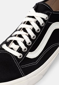 Sapatilha preta em lona com detalhes brancos, apresentando um design clássico de atacador, ilhós reforçados e costura em contraste ao longo dos lados.