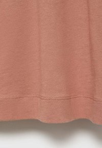 Katoenen T-shirt in een zachte perzikkleur met een gladde textuur, voorzien van een afgeronde zoom en subtiele stiksels langs de rand.