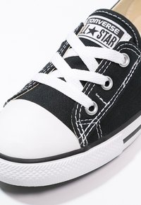 Svart canvas sneaker med vit gummikappa, kontrasterande vita snören och sydda detaljer. Har en svart och vit etikett på tungan.