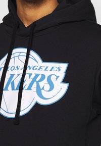Czarna bluza z kapturem z dużym białym i niebieskim logo "Los Angeles Lakers" oraz grafiką kosza. Widziane są sznurki z czarnymi końcówkami.
