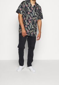 Kortärmad svart blommig skjorta med gröna blad och rosa blommor, i kombination med mörka byxor och vita sneakers. Avslappnad passform och lättviktig tyg.