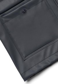 Gros plan d'une poche de veste en cuir gris foncé avec des coutures apparentes et une fermeture à bouton-pression noire.