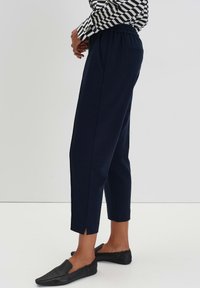 Pantaloni a vita alta navy con cintura elastica, tasche laterali e piccoli spacchi all'orlo, abbinati a scarpe nere da indossare senza lacci.