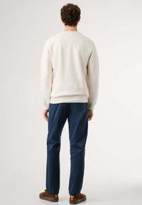 Sudadera blanca con puños y dobladillo acanalados, combinada con pantalones azul marino. La tela parece suave y ligeramente texturizada.
