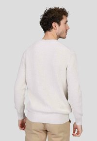 Pull en crème à côtes avec un col rond et des manches longues. Présente une texture douce et un ourlet ajusté. Vu de derrière.