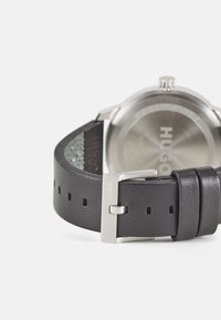 Schwarzes Lederarmband mit silberner Metallschnalle, mit Perforationen zur Anpassung und einem Gehäuseboden aus rostfreiem Stahl.
