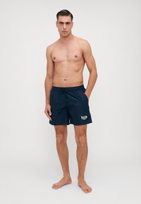 Shorts de baie navy cu talie elastică și șnur, având un imprimeu alb cu logo pe piciorul stâng. Material neted și ușor.