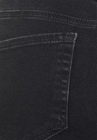 Jeans de mezclilla negros elásticos con un bolsillo trasero, costuras visibles a lo largo de las costuras y un acabado de tela suave y ligeramente texturizado.