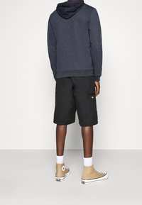 Felpa della marina con cappuccio a fantasia, abbinata a pantaloni corti neri. Sneakers alte color carne e calzini bianchi a maniche corte sono visibili. Design semplice e casual.