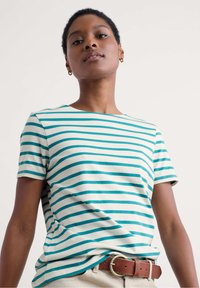 Camiseta de algodón con rayas en tonos verde azulado y blanco, cuello redondo, mangas cortas y corte relajado. Combinada con un cinturón marrón.