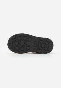 Suela de zapato de goma negra con un patrón de tracción en forma de estrella, que incluye una sección lisa cerca del talón y una marca de impresión.