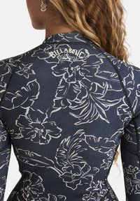 Námořnický květinový rash guard s bílým květinovým potiskem, dlouhými rukávy a zipem na zadní straně. Obsahuje značkové logo na krku a kontrastní švy.