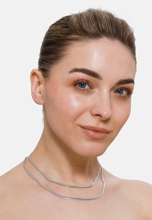 Collier en argent superposé avec un design lisse et courbé. Comprend deux brins : l'un plat et texturé, l'autre légèrement arrondi et brillant.