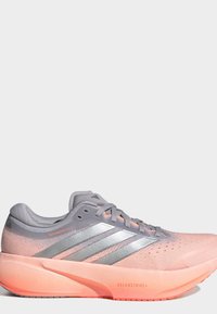 Ροζ ανοιχτό και γκρι παπούτσι για τρέξιμο Adidas με ασημένιες ρίγες και χοντρή ροδακινί σόλα με ετικέτες Dreamstrike+ και Supernova Rise 3.