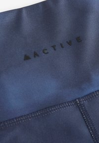Mornje plave sportske tkanine s glatkom teksturom s tiskanim logotipom "ACTIVE" u crnoj boji. Vidljivi šavovi na donjem rubu.