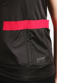 GORE cykelkläder topp i svart tyg med ett rött horisontellt streck, med en ficka med dragkedja och logodetaljer i botten.