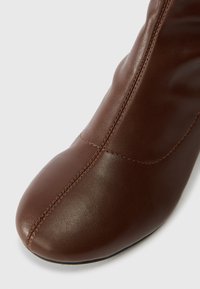 Brown leather ankle boot with a smooth texture, pointed toe, and contrasting stitching along the side, showcasing a sleek design.