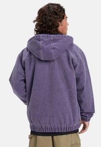 Purple hooded jacket with a relaxed fit, featuring elastic cuffs and hem, visible stitching, and a soft, textured finish.