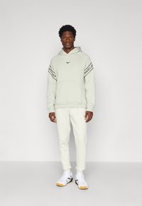 Jasnoszary hoodie z czarnymi akcentami, przednią kieszenią i logo. W zestawie z pasującymi jasnoszarymi dresami i białymi trampkami z czarnymi oraz żółtymi detalami.