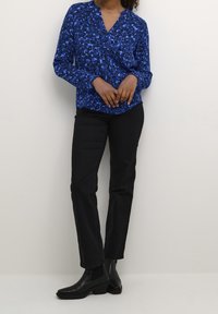 Blusa blu con motivo, scollatura a V, maniche lunghe e vestibilità rilassata, abbinata a pantaloni neri slim-fit e stivali alla caviglia.