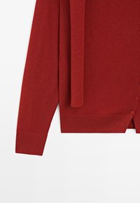 Red long-sleeve knit sweater with ribbed cuffs and hem, featuring a side button detail and attached matching belt.