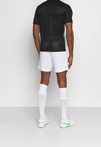 Czarny sportowy t-shirt z krótkimi rękawami i fakturowanym tyłem, w połączeniu z białymi szortami i białymi skarpetami do kolan. Zielone akcenty na korkach.