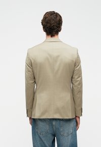 Ανοιχτό μπεζ σακάκι με υφή, μονό άνοιγμα και κλείσιμο με δύο κουμπιά. Συνδυασμένο με φαρδιά μπλε τζην παντελόνια.