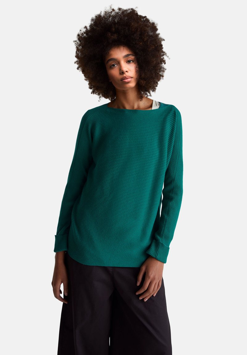 Miętowy prążkowany sweter z dekoltem w łódkę, długimi rękawami i luźnym krojem, zestawiony z czarnymi spodniami o szerokich nogawkach. Gładka tekstura na całej powierzchni.