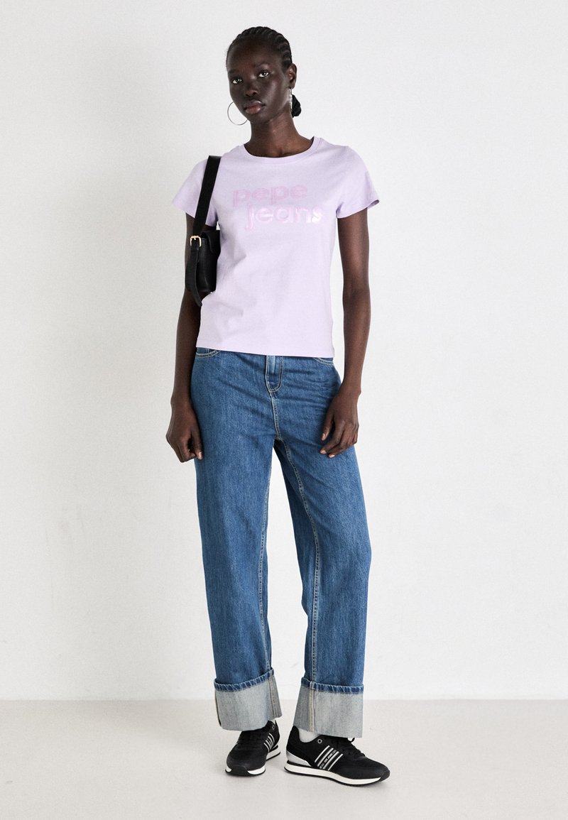 T-shirt à manches courtes lavande avec le texte "Pepe Jeans" ; associée à un jean en denim bleu large et des baskets noires. Un sac à bandoulière noir est inclus.