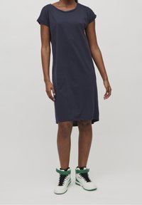 Robe t-shirt en coton bleu marine avec des manches courtes retroussées, un col rond et des fentes sur les côtés. Associée à des baskets montantes blanches avec des accents verts.