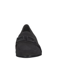Scarpa slip-on in suede nera con punta arrotondata, caratterizzata da una fascia decorativa e dettagli in metallo sulla parte centrale del piede. Suola piatta, texture liscia.