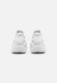 Valkoiset urheilukengät, joissa on sileä päällinen, teksturoitu verkkovuori ja pehmustettu pohja, joka sisältää erottuvan muotoilun ja hillityn logon yksityiskohdan.