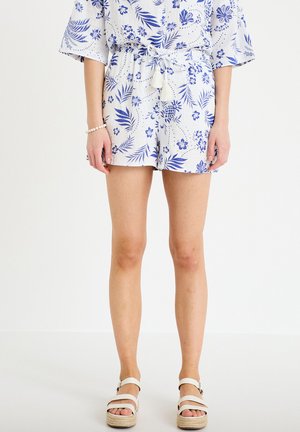 Pantaloncini bianchi con motivi floreali e di ananas blu, vita elastica con coulisse, indossati con sandali bianchi e top abbinato.