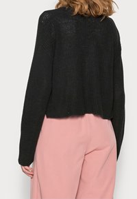 Maglione nero a maglia corto con texture a coste e maniche lunghe, abbinato a pantaloni rosa a gamba ampia. Il maglione ha un collo arrotondato.
